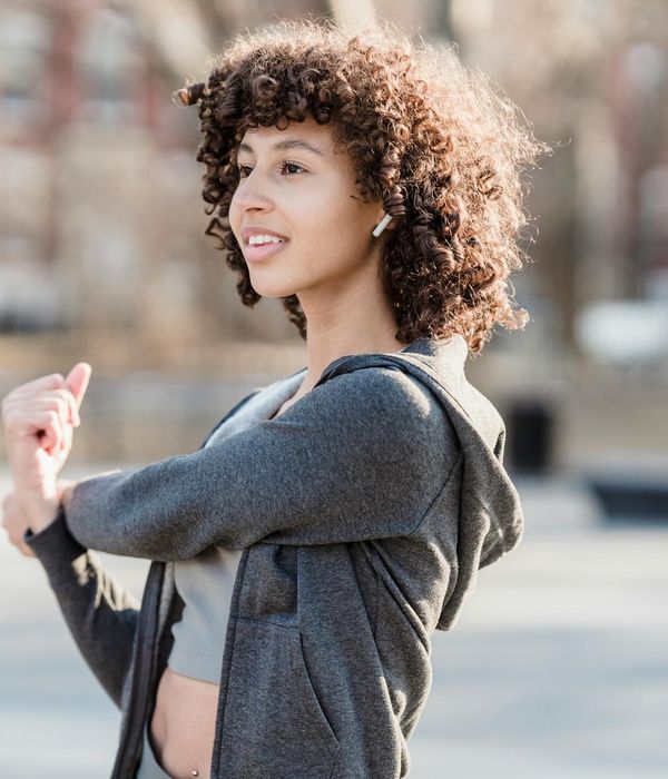 Woman smiling and stretching outdoors in a sunny park.